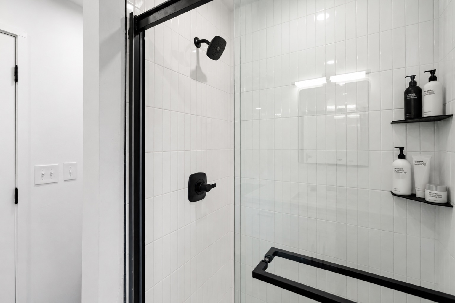 Shower at Unit A with stacked white tile and matte black fixtures